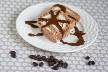 Coffee Swiss roll two slices drizzled with dark chocolate on glass decorated white plate, spilled fresh coffee beans