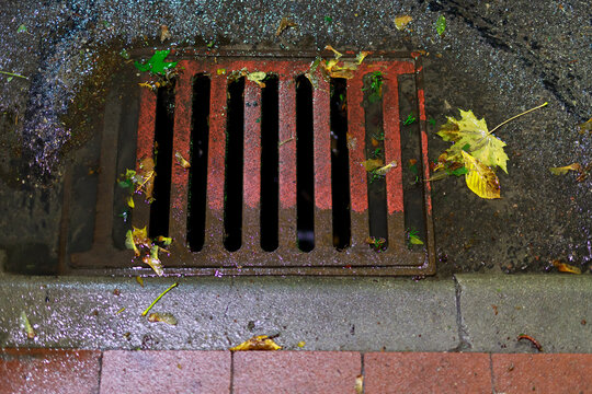 Thick and solid sewer drain embedded in the road. Rainwater flowing down the way to the sewer drain.