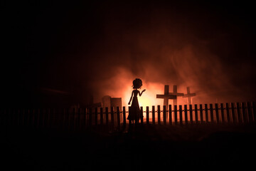 Obraz na płótnie Canvas Girl walking alone in the cemetery at night. Dark toned foggy background. Horror Halloween concept