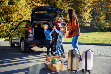 High-spirited likable parents unloading the auto's trunk with their cute 10-12s kids during moving...