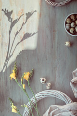 Easter flat lay with quail eggs, yellow freesia flowers and rattan wreath.