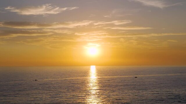 El sol entre las nubes al atardecer y su reflejo sobre el mar con dos canoas acerc&aacute;ndose a la estela dorada  en C&aacute;diz, Andaluc&iacute;a, Espa&ntilde;a.