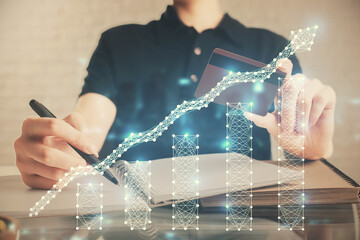 Double exposure of man hands holding a credit card and Forex graph drawing. Stock trading and digital fintech in Internet E-commerce concept.