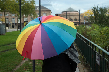 Portrait on back view of woman walking in the street with a rainbow umbrella