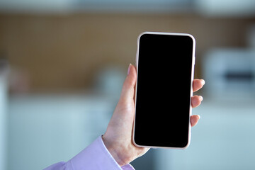 Close-up of a phone with an empty black screen on a blue blurry background. Beautiful well-groomed hands.