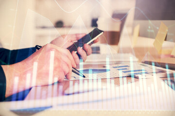 Double exposure of man's hands holding and using a phone and financial graph drawing. Analysis concept.