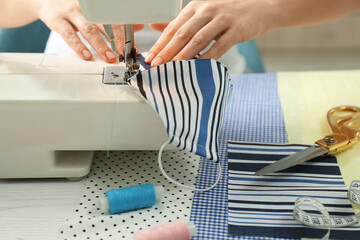 Woman sewing cloth mask with machine at table, closeup. Personal protective equipment during COVID-19 pandemic