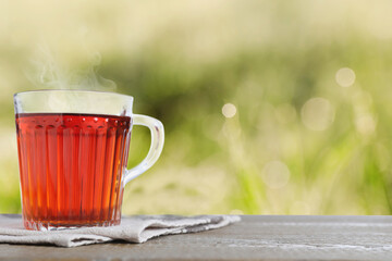 Glass cup of fresh hot tea on wooden table against blurred green background. Space for text