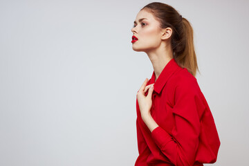 A beautiful girl with red lips and a shirt on a light background gestures with her hands