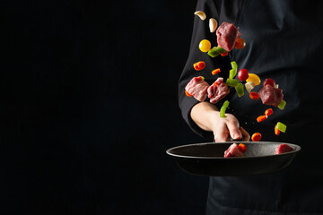The professional chef tossed fresh pork with vegetables in frying pan on black background....