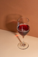 Wineglass with fragrant red wine on beige background with shadow on the wall. Wine time. Concept of festive evening.