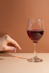 Wineglass with tasty red wine with girl's hand background. Beige surface. Festive concept.