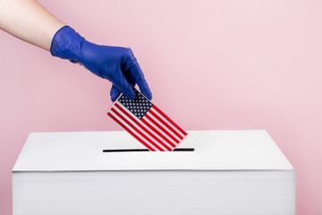 Woman in blue protective gloves puts the USA flag in voting box. Elections and coronavirus concept.