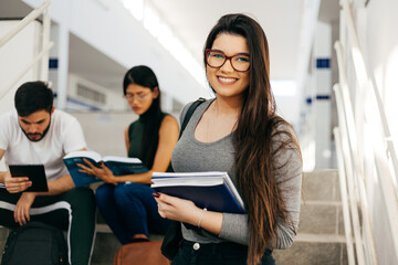 Portrait of young Brazilian student with backpack carrying books in college.