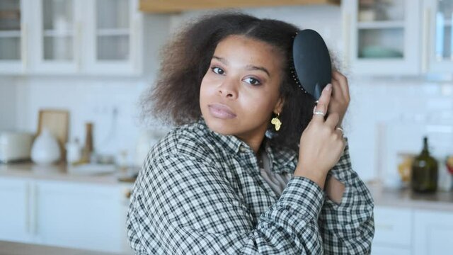 charming african american woman combing her hair while standing in the kitchen