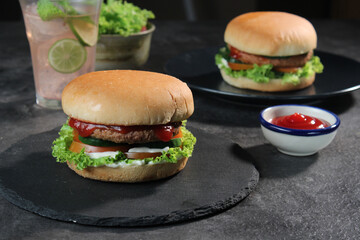 Two delicious fresh meat burgers with tomato sauce and vegetables on a dark background.
