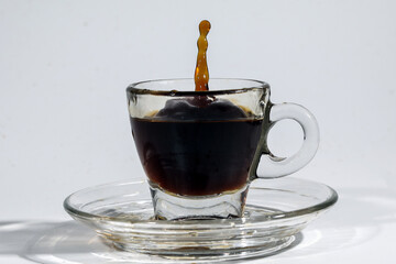 Coffee splash pillar in transparent glass espresso cup saucer full of liquid coffee on white background