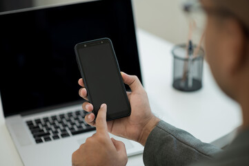 Close up male hands using smartphone and laptop while work from home social distancing concept. Focusing Finger texting on cell phone.