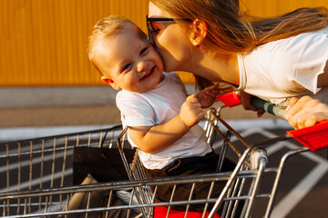 Happy family, mom makes purchases with a little child sitting in a shopping cart on the street...