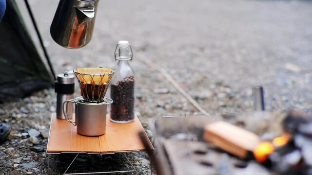 キャンプ場でコーヒー豆を挽いてコーヒーを入れて飲む一人の男性
