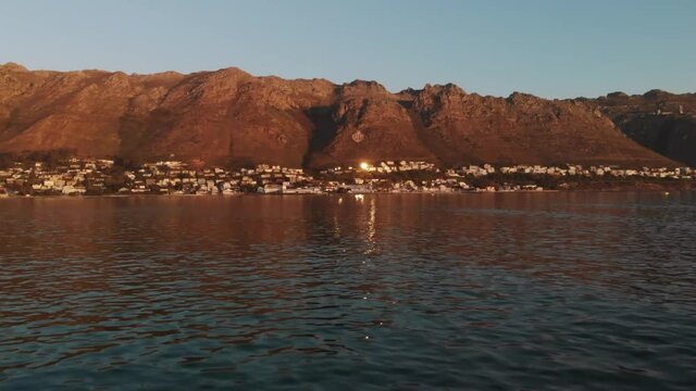 A beautiful shot over the ocean coming towards a town with a mountain range behind it