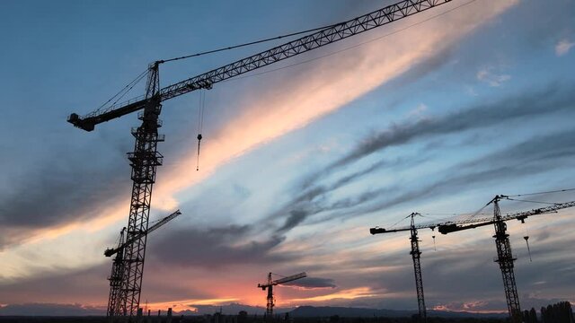 Silhouettes of Construction Cranes Under Colorful Sunset Sky. New Real Estate Development or Economy Loss Concept