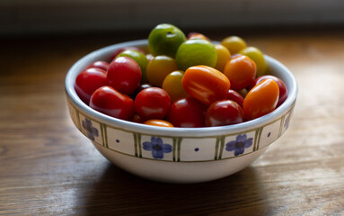 A slightly elevated view of a small white with blue patterned ceramic bowl with a colorful mix of plum and cherry tomatoes on a wooden kitchen counter

