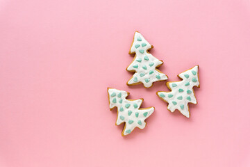 Homemade christmas gingerbread cookies in the shape of trees on a pink background, space for text