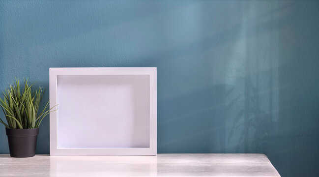 Mockup white wooden picture frame and houseplant on white top table with blue wall, copy space.