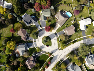 Overhead aerial view of colorful autumn trees residential houses and yards along suburban street