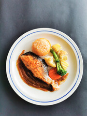 salmon steak with bread and vegetables on round plate and black background, vertical photo