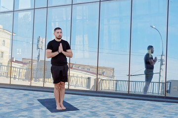 Fototapeta na wymiar Man athlete in black sportswear practices yoga exercises prayer position. Hands in namaste posture.