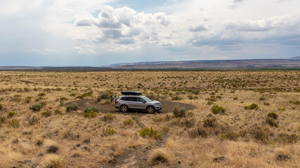 Diamond Craters Loop, Oregon / USA - 23 July 2020: Honda Pilot with mounted Yakima roof box and bikes on a bike rack on the road in the middle of a desert landscape against gloomy rainy sky.