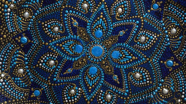 Decorative ceramic plate with black, blue and golden colors, painted plate rotating on background, closeup, top view. Decorative porcelain plate painted with acrylic paints, handwork, dot painting