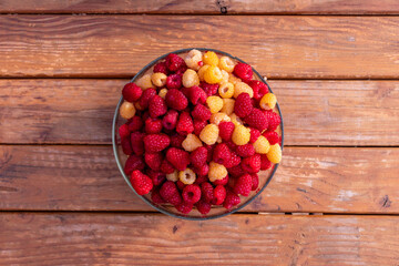 Top to down view at glass bowl full of ripe delicious white and red raspberries on a wooden table