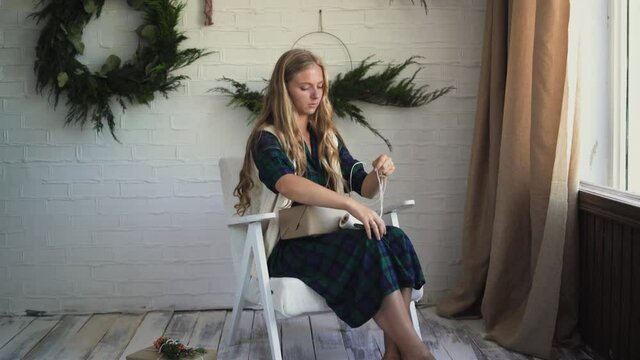 young beautiful woman is sitting in an armchair and packing a gift.