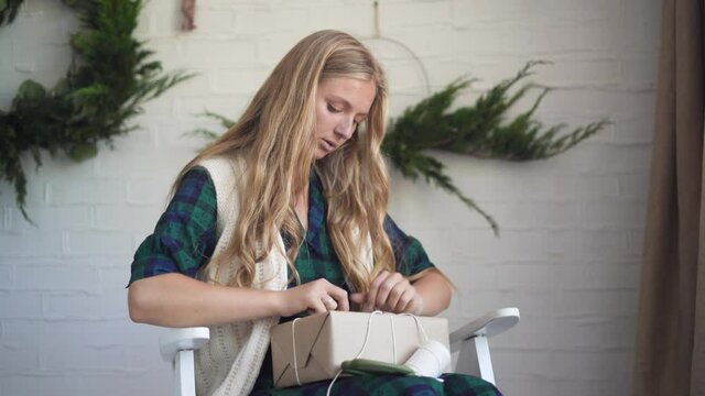 close-up portrait of a young woman, sitting on an armchair, decorates a box with a gift