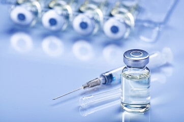 Single use syringe for injection treatment on medical table with vials of liquid drug doses flu...