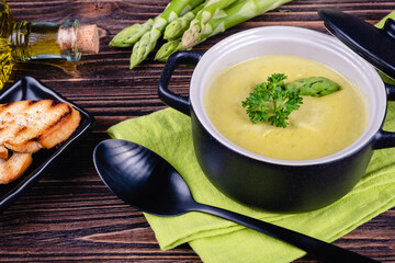 Fresh asparagus creamy soup and ingredients on a wooden table.