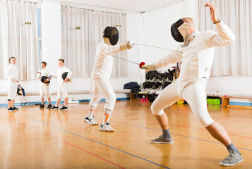 Athletic group practicing effective fencing techniques in sparring in training room