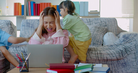 Seriously young mother working at home with two daughters naughty