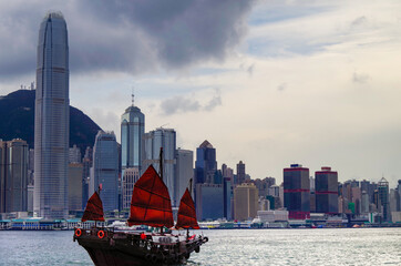 Traditional Chinese junk with red sails in Victoria Harbor, Hong Kong in China with panoramic city...