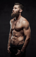 Cool and haired shirtless man with beard and moustache in pants posing with hands in pockets in...