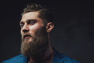 Closeup photography in side view of brutal businessman in blue suite with beard and stylish haircut...
