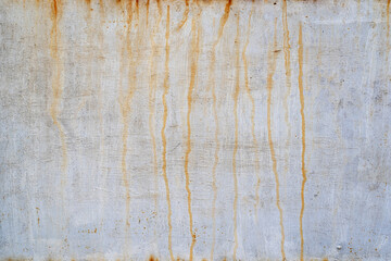 Old steel sheet wall covered with white paint. There are orange-colored rust streaks. Background....