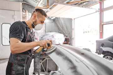 The mechanic works with a grinding tool. Sanding of car elements. Garage painting car service....