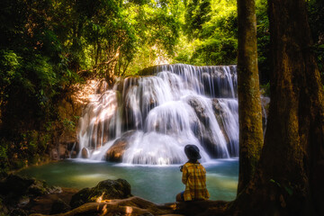 Young woman sitting on the rock and enjoying waterfall landscape. Travel concept adventure Huay Mae Khamin Waterfall Thailand