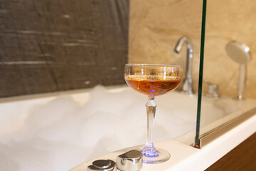 Glass of drink by the bathtub full of foam