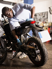 Fototapeta na wymiar Afro american man working at restoring motorbike in motorcycle workshop. High quality photo