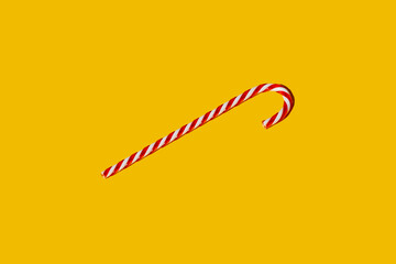 Christmas symbol. Peppermint candy cane. Festive lollipop. Winter holidays decoration. White red striped sugar stick isolated on bright yellow copy space background.